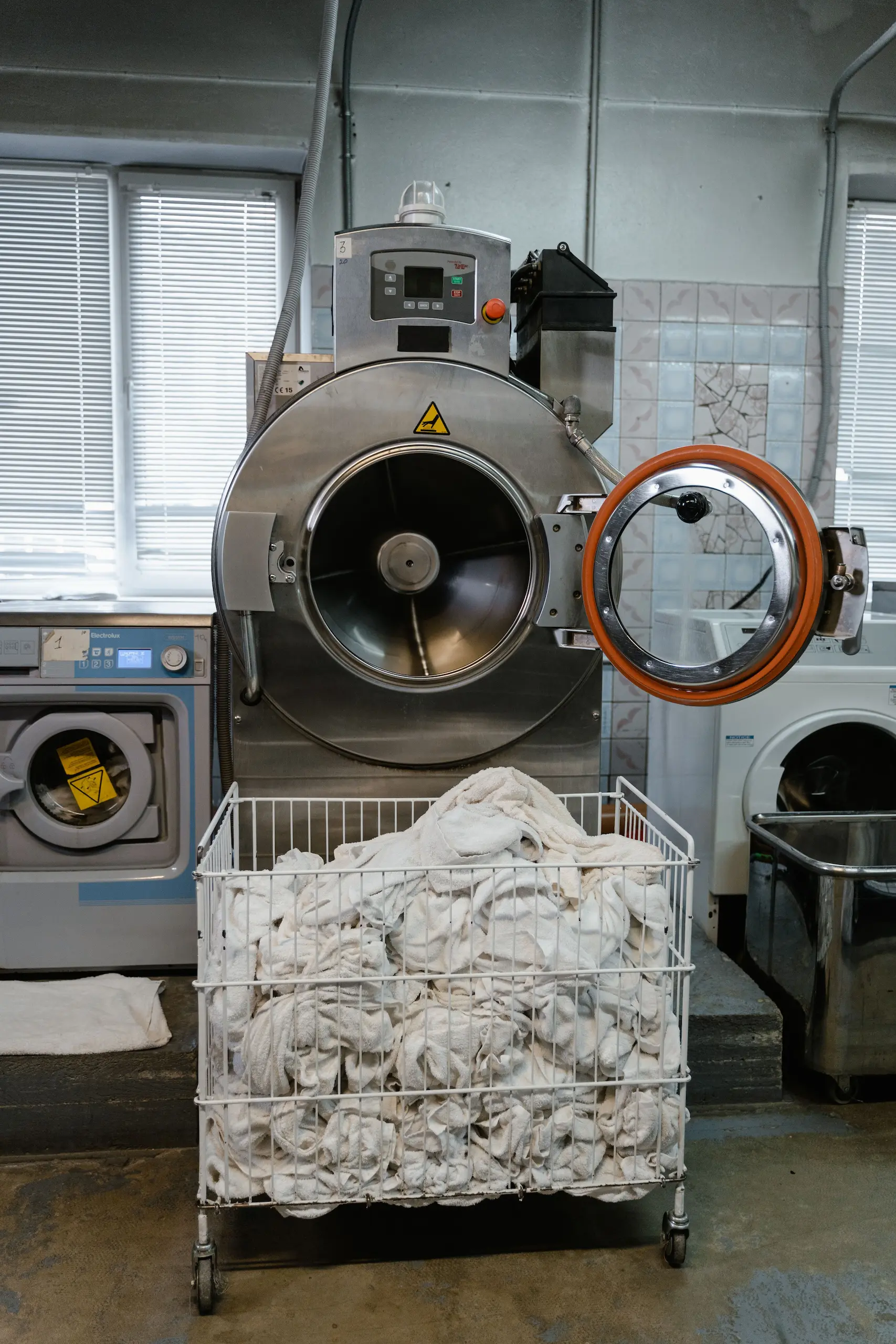 Large commercial washing machines with a trolley of neatly folded white clothes